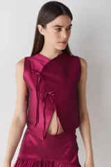 Top sin mangas de estilo cruzado, confeccionado en tela satinada color bordó. Presenta un cierre frontal mediante lazos finos y un diseño corto que deja ver parte del abdomen.