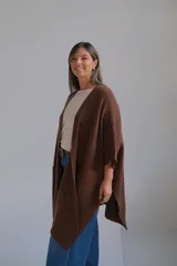 Poncho abierto de color marrón chocolate, con diseño de corte asimétrico, mangas amplias y bolsillos frontales aplicados.