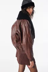 Campera de cuero marrón con cuello solapa, corte holgado y cierre frontal con un botón.