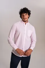 Camisa de manga larga confeccionada en tejido poplin con diseño de rayas verticales finas en color rosado y blanco. Presenta cuello abotonado (button-down), cierre frontal con botones y un bolsillo en el pecho.
