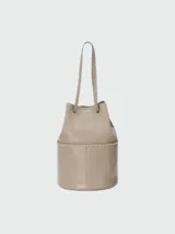 Bolso tipo bucket de cuero color beige con tachas plateadas en la parte inferior y doble asa de mano.
