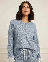 Pijama de dos piezas compuesto por una remera de manga larga con cuello redondo y cierre frontal de botones, y un pantalón con cintura elástica ajustable mediante cordón. Presenta un estampado texturizado en tonos azules y detalles de puños con diseño geométrico.