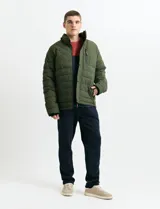 Campera acolchada de color gris, con capucha desmontable, cierre frontal y bolsillos laterales con cremallera. Presenta un diseño de costuras horizontales y detalles en color naranja en los tiradores de los cierres.