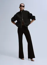 Chaqueta negra de diseño estructurado, con cuello alto, cierre frontal de cremallera metálica y mangas abullonadas con puños ajustados.