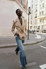 Blazer cruzado color beige, de manga larga, con cuello solapa y forro interior negro. Presenta cierre frontal con botones dorados y bolsillos de vivo en el pecho y bolsillos con solapa en el delantero.