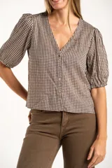 Blusa de algodón con estampado de cuadros vichy en tonos negro y blanco. Presenta escote en V, cierre frontal con botones y mangas cortas abullonadas con terminación elástica.