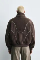 Cazadora de corte relajado confeccionada en tejido de borreguillo con diseño de paneles en tonos marrón y beige. Presenta cuello subido, cierre frontal de cremallera, bolsillos laterales y acabados en rib en puños y cintura.