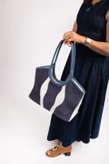 Bolso tipo tote de tela color crudo con detalles de cuero marrón en las asas y la base.