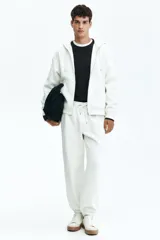 Pantalón deportivo de felpa color blanco roto, con interior cepillado suave. Presenta elástico revestido y cordón ajustable en la cintura, bolsillos laterales y puños acanalados. Corte relajado.