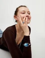 Anillo de aleación de metales con baño de plata de ley, presenta un cristal facetado de color azul en talla ovalada engastado en el centro.