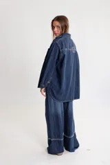 Camisa de jean azul oscuro, de corte oversize, con mangas largas y puños abotonados. Presenta bordados rojos en el pecho y un parche denim con el logo "BG" en la espalda.