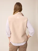 Chaleco de sherpa color beige con cierre frontal completo, cuello alto y bolsillo con cierre en el pecho que incluye un detalle circular con logo.