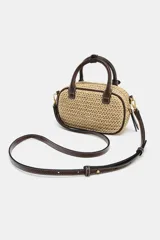 Bolso pequeño tipo bowling de rafia tejida en color natural, con ribetes, asas de mano y detalles en cuero marrón oscuro. Incluye un charm colgante con candado dorado y una correa ajustable extraíble para llevar al hombro o cruzado.