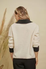Saco de punto color crema con cuello, puños y detalle en el bolsillo en color negro. Presenta cierre frontal con botones dorados y diseño de corte recto.