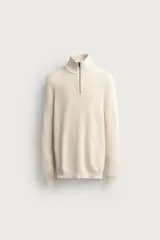 Jersey de punto perlado en hilatura de algodón, color beige, con cuello perkins y cierre frontal de cremallera corta. Cuenta con manga larga y acabados en rib.