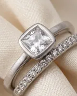 Anillo de acero con piedra central cuadrada y circonitas incrustadas en el aro.