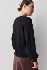 Sweater negro de tejido suave con escote redondo, mangas largas y calce relajado, con terminaciones acanaladas en cuello, puños y ruedo.