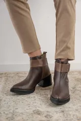 Bota corta de cuero negro con acabado combinado mate y charol. Presenta una tira decorativa con tachas metálicas y hebilla en el tobillo, tacón cuadrado robusto y suela con plataforma.