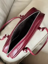 Cartera de mano tipo bowling color bordó, confeccionada en material sintético con textura arrugada. Cuenta con doble asa fija y cierre superior.