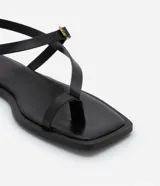 Sandalias planas de cuero sintético negro, con puntera cuadrada, tira delantera con dedera y tira trasera con hebilla metálica dorada.