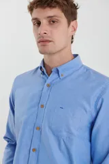 Camisa de vestir blanca de manga larga, con cuello abotonado, bolsillo frontal y botones en tono madera.