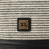 Bandolera de diseño tipo cubo, confeccionada en una combinación de rafia con patrón de tejido en zigzag blanco y negro, y base de cuero sintético negro. Presenta una placa metálica dorada con el logo de la marca en el frente y una correa fija de cuero sintético negro.