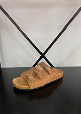 Sandalias de tres tiras ajustables con hebillas metálicas plateadas, confeccionadas en material simil gamuza, con plantilla anatómica y suela de corcho.