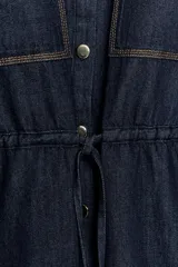 Camisa de denim azul oscuro con cuello solapa, mangas amplias por debajo del codo y bolsillos de parche en el frente. Cuenta con cintura ajustable mediante cordón y cierre frontal con botones metálicos.