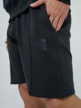 Bermuda de felpa de algodón color celeste, con bolsillos laterales y detalle de costuras verticales al frente. Presenta un parche distintivo de la marca en la pierna izquierda.