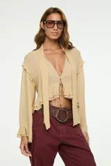 Blusa color tostado con escote en V profundo, volados en la parte inferior y en las mangas largas amplias, y un lazo frontal ajustable.