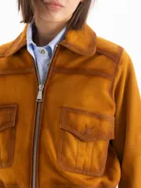 Campera bomber confeccionada en gamuza color tostado, con cierre frontal, bolsillos aplicados con solapa en el pecho y puños y cintura tejidos en marrón oscuro.