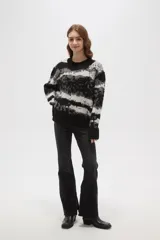Sweater de tejido jacquard con diseño de rayas irregulares en tonos negro, blanco y gris. Presenta cuello redondo a la base, mangas largas y un corte holgado.