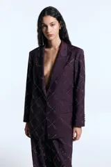 Blazer de sarga color bordó con corte oversize, hombreras marcadas y cierre frontal con un botón forrado a tono. Presenta un diseño estampado de cuadrícula con detalles de hotfix y bolsillos frontales con solapa.