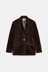 Blazer de piel 100% color marrón oscuro, con cuello solapa, manga larga con hombreras y bolsillos delanteros con solapa. Presenta pespuntes decorativos en contraste y cierre frontal con un botón.