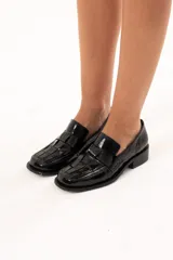 Mocasín de cuero charol negro con diseño enrejillado en la capellada, horma cuadrada y taco bajo.