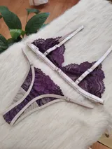 Conjunto de lencería compuesto por un bralette triangular y una bombacha tipo tanga, confeccionados en encaje color violeta con terminaciones y breteles en color tostado.
