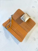 Billetera grande de cuero con acabado metalizado dorado y textura tipo reptil. Cuenta con un compartimento frontal con solapa y cierre a presión, decorado con el logo de la marca grabado.