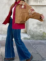 Campera tipo bomber color camel, confeccionada en gamuza, con bordados decorativos en tonos natural y bordó en las mangas y hombros. Presenta cierre frontal y diseño holgado.