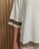Buzo de punto negro con diseño holgado, mangas codo y detalles en tono tostado y blanco en el cuello redondo, puños y ruedo.