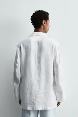 Blazer de corte relajado confeccionada en tejido de lino. Presenta cuello chal, manga larga, bolsillos de plastrón en la parte frontal y cierre cruzado con botones.