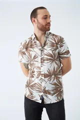 Camisa de manga corta con estampado de hojas en tonos marrones sobre fondo blanco. Presenta cuello clásico, cierre frontal abotonado y logo bordado en el pecho.