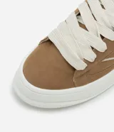 Championes de estilo skater para hombre, confeccionados en poliuretano color marrón oscuro. Poseen punta redonda, caña baja y suela de plataforma blanca. Destacan por sus cordones anchos tipo fat lace y detalles laterales en contraste.