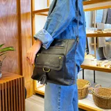 Bandolera negra de cuero sintético con cierre superior y correa larga regulable. Tiene bolsillo frontal con tapa y broches magnéticos, detalle de trenza artesanal, división interna, bolsillos internos y bolsillos laterales tipo ojal.