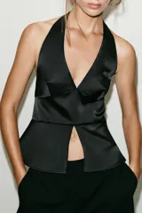 Top halter satinado negro con escote en V profundo, espalda descubierta, bajo en evasé con abertura frontal y cierre lateral con cremallera oculta.
