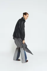 Chaqueta negra de piel 100% con cuello alto, manga larga con puño, bolsillos delanteros y cintura ajustable con cordón elástico y stopper. Cierre frontal con cremallera metálica y botones a presión ocultos por solapa.