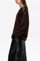 Jersey de punto color marrón con detalles de encaje negro aplicados en el hombro y lateral. Presenta cuello redondo, manga larga y corte holgado.