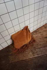 Maxi cartera tipo bolso color marrón claro, confeccionada en cuero gamuza natural sin forro. Presenta flecos colgando en toda su base y llavero interno con gancho.