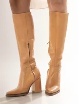 Botas de cuero color caramelo, de caña alta, con punta fina y taco geométrico.