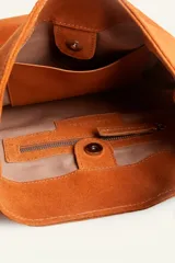 Cartera tipo balde color tostado, confeccionada en gamuza, con correa ajustable decorada con tachas metálicas plateadas.