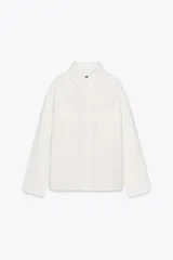 Sobrecamisa blanca de algodón con cuello solapa, manga larga y dos bolsillos de plastrón en el pecho. Cierre frontal con botones ocultos por solapa.